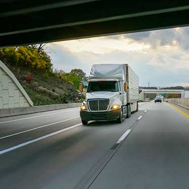 white semi-truck passing under highway bridge