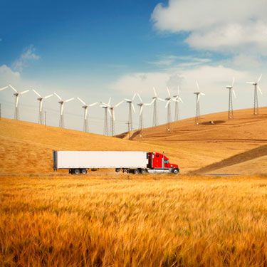 semi-truck driving on road between field of wind turbines