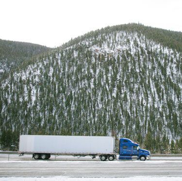 Freight Shipping from Oklahoma to Texas - Blue truck on highway along snowy hill