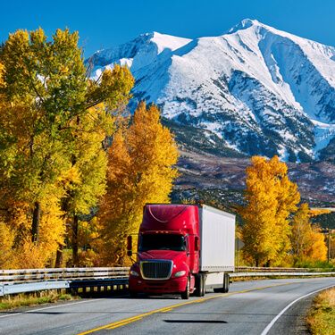 Freight Shipping from Oklahoma to Colorado - Red semi truck by foliage near mountains