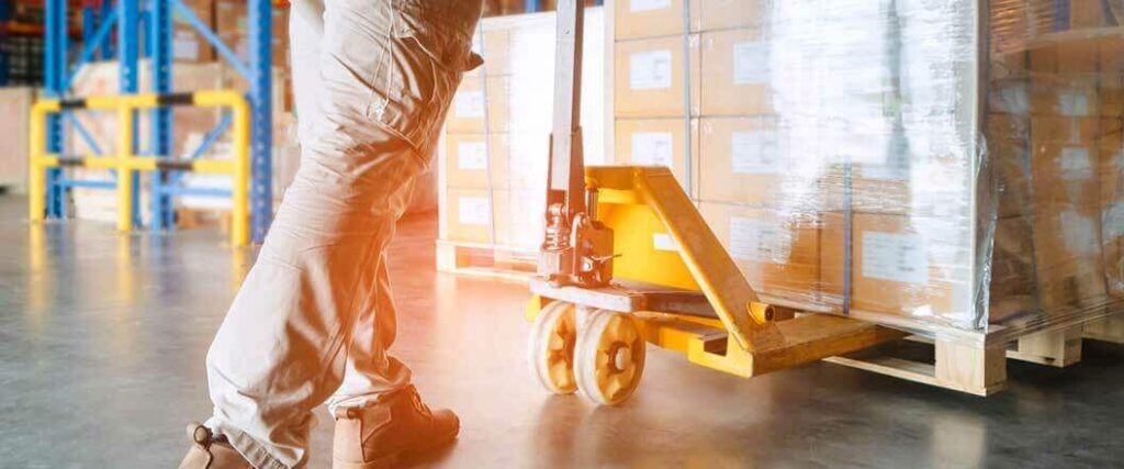 A warehouse worker moving a palletized load in a warehouse with a pallet jack
