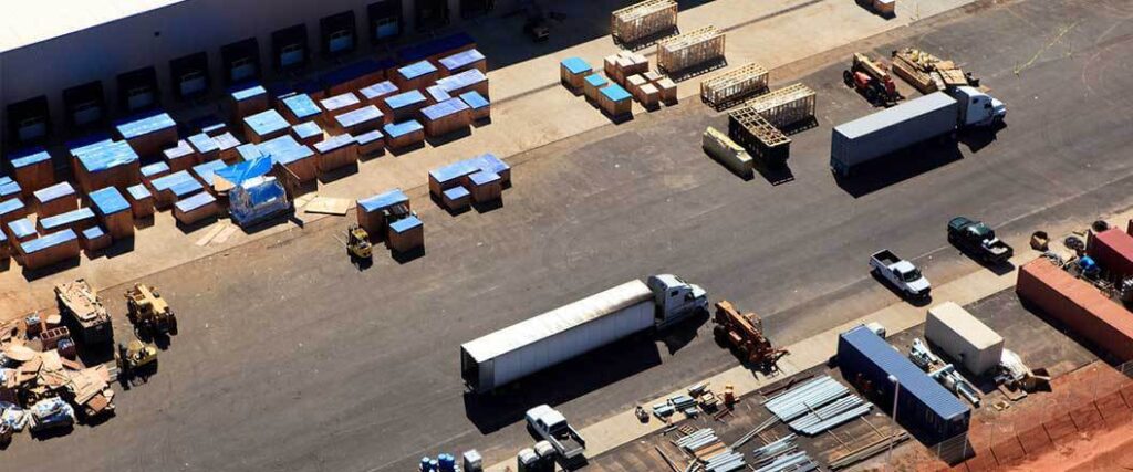 An isometric view of semi trucks, forklifts, cargo containers, and pickup trucks at a distribution center.