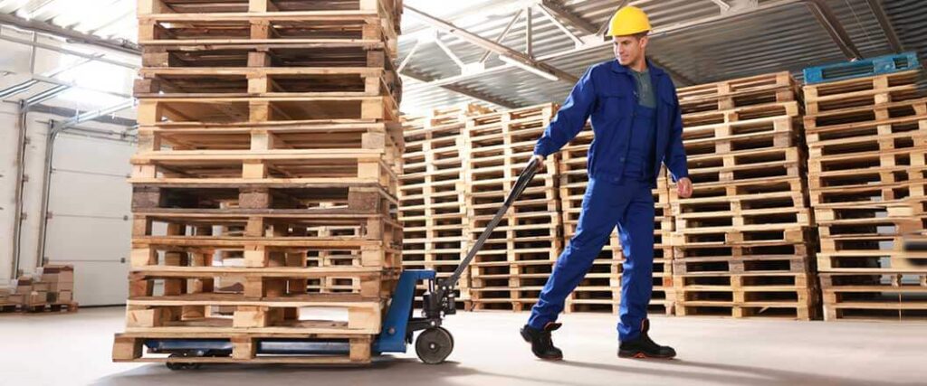 A warehouse worker pulling stacked pallets on a pallet jack